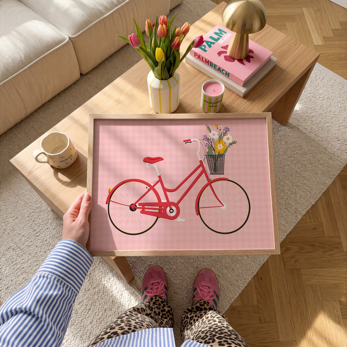 An illustrated print of a red bike with a basket, which is full of bright colourful flowers. The background of the print is a warm pink gingham pattern.
