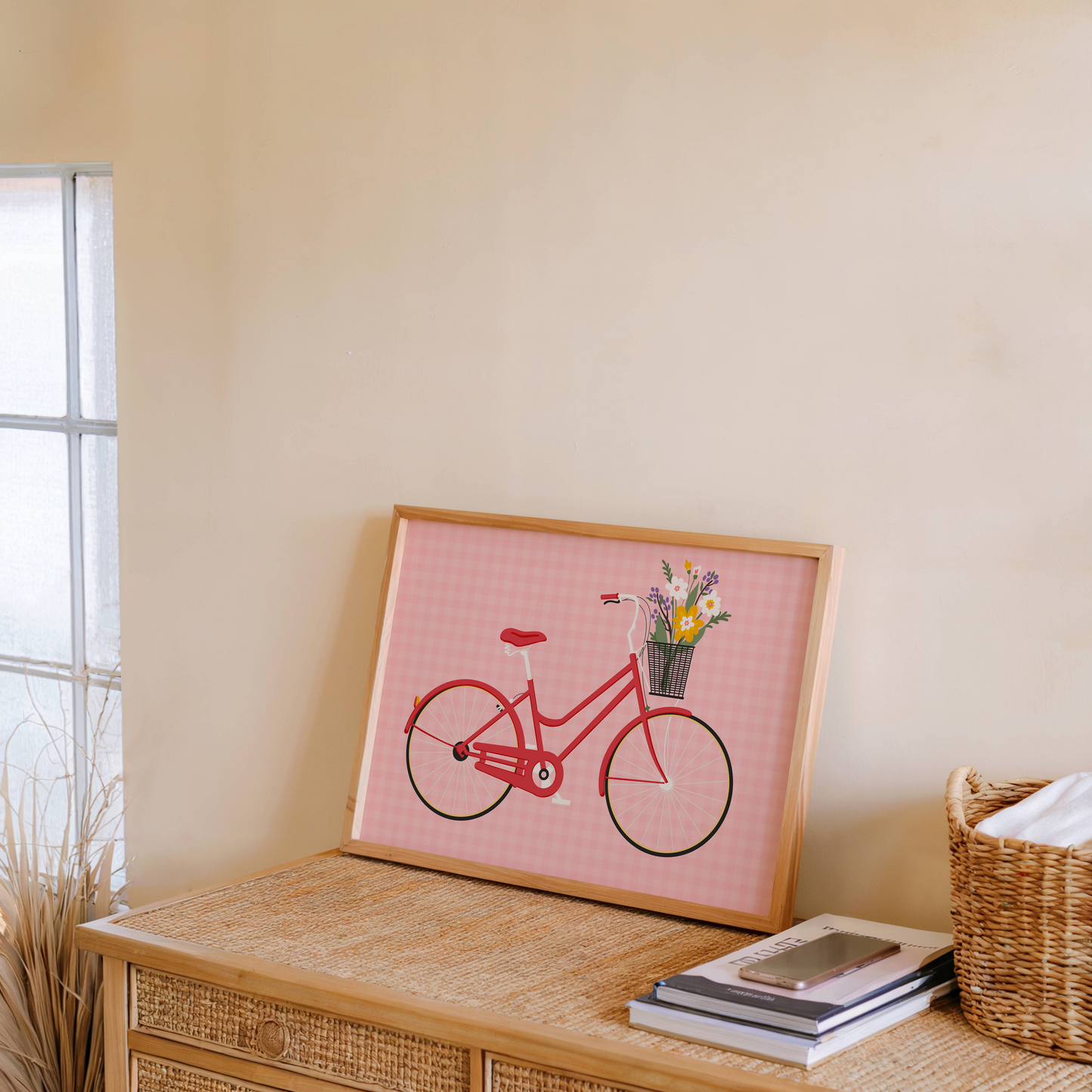 An illustrated print of a red bike with a basket, which is full of bright colourful flowers. The background of the print is a warm pink gingham pattern.
