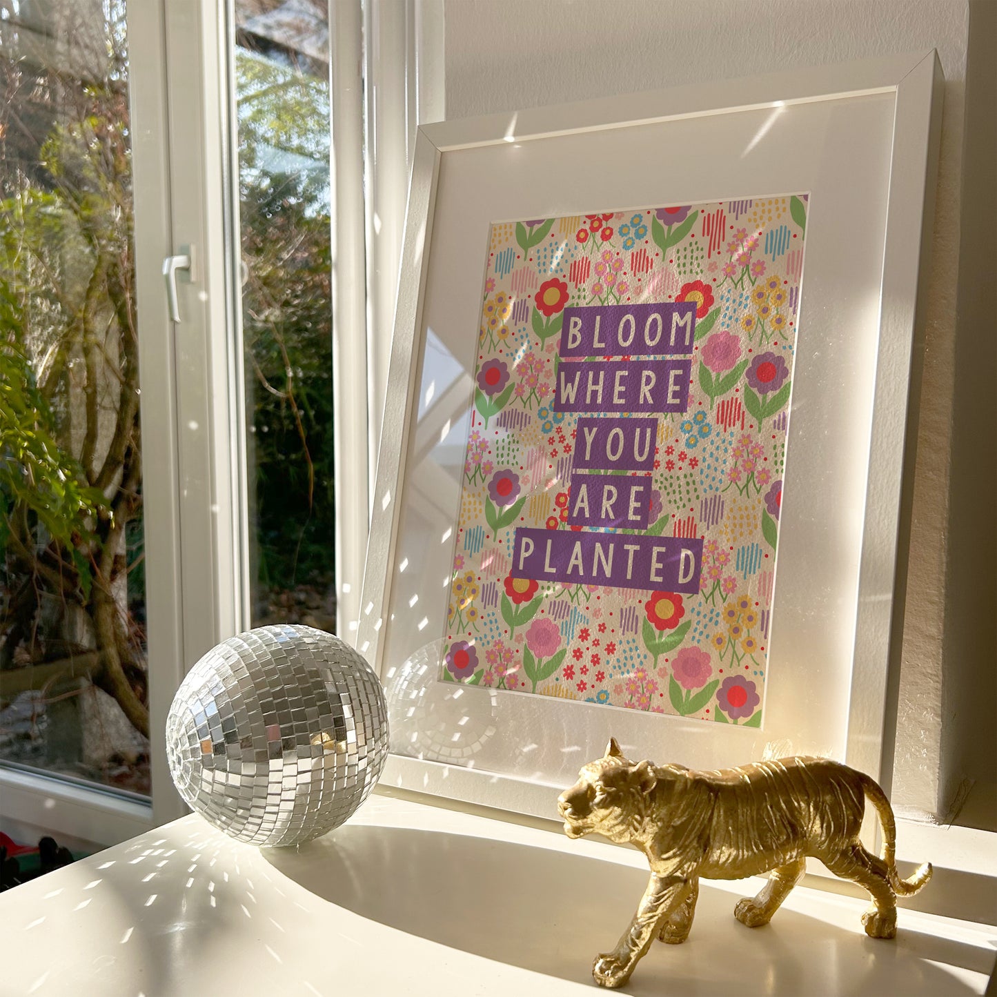 A colourful illustration of a floral background with purple text saying bloom where you are planted.