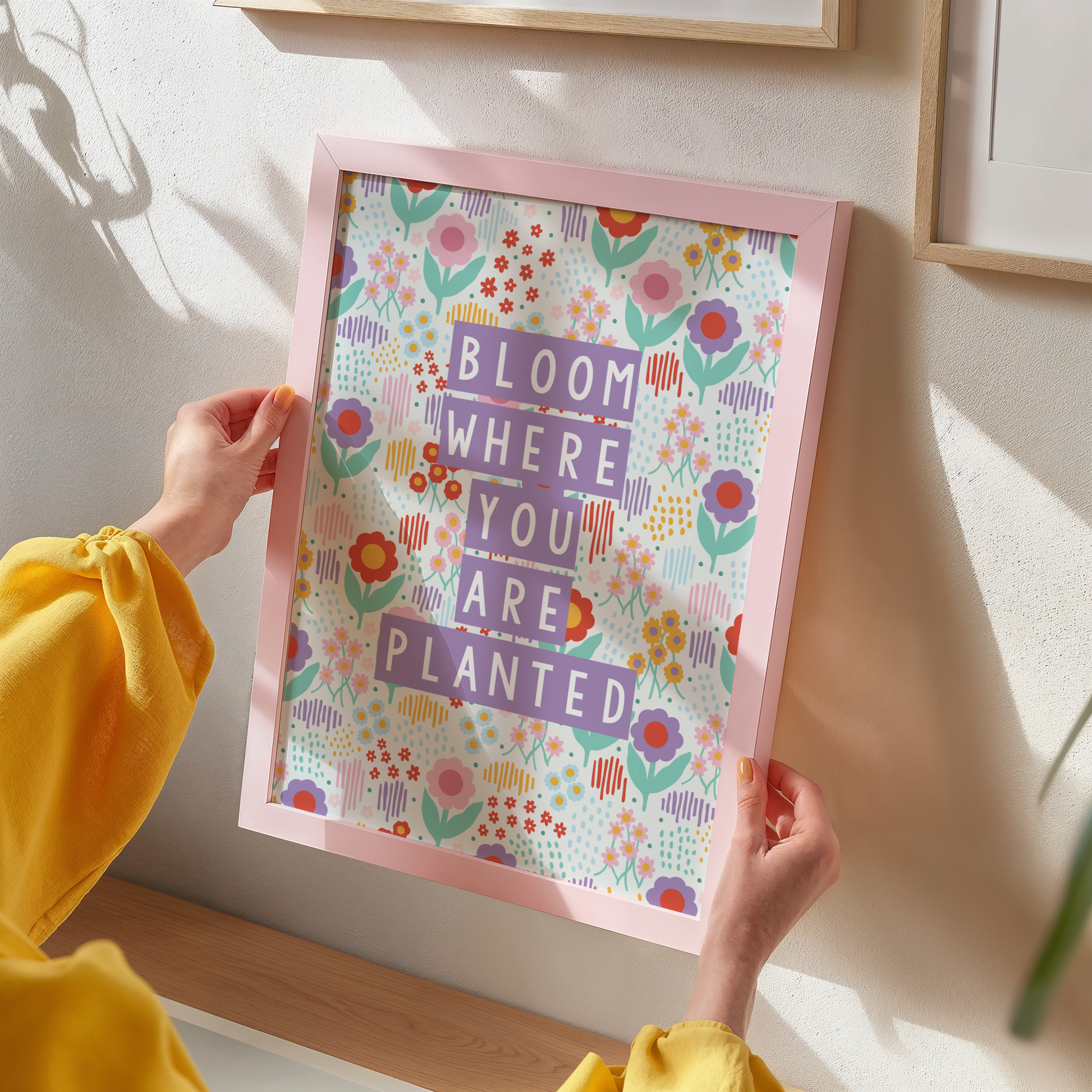 A woman's hands holding a pink framed print of a colourful floral illustration quote.