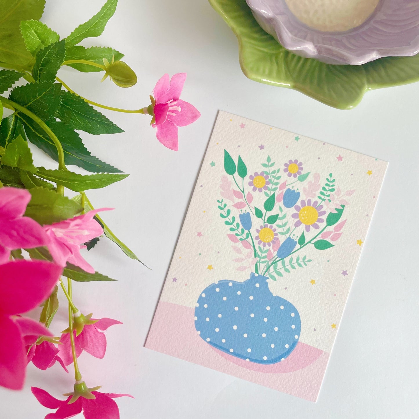 A textured postcard, featuring a blue vase with multicoloured flowers in it.