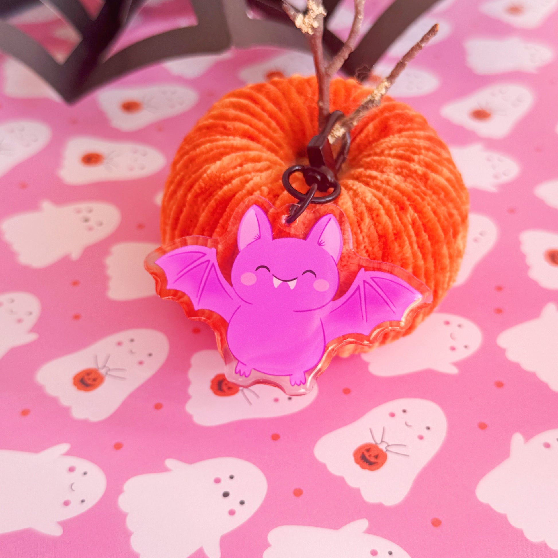A purple acrylic bat keyring, featuring an illustration of a  cute smiling bat. The keyring has a black clasp to attach it to keys or a bag.