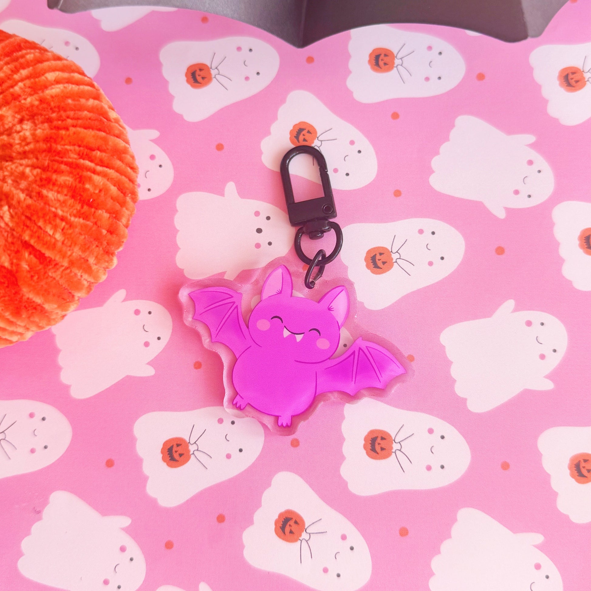 A purple acrylic bat keyring, featuring an illustration of a  cute smiling bat. The keyring has a black clasp to attach it to keys or a bag.