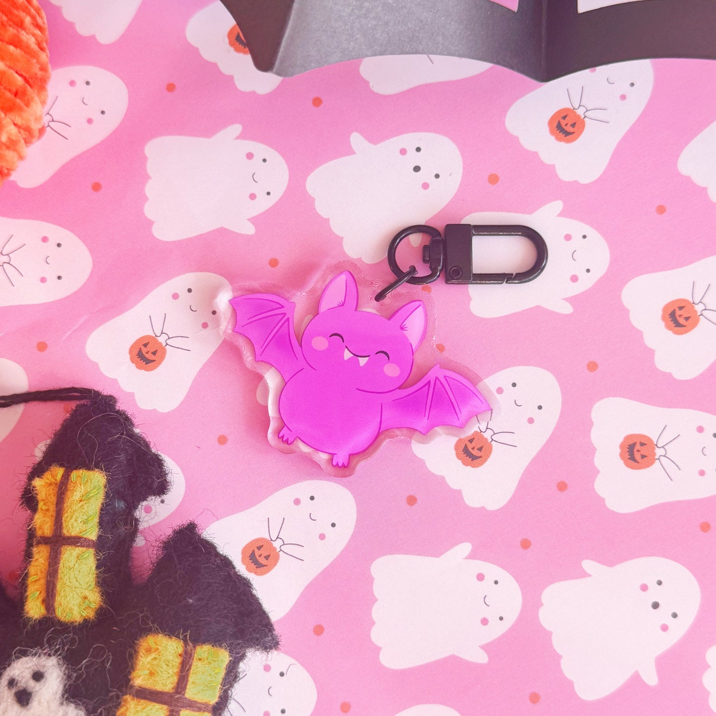 A purple acrylic bat keyring, featuring an illustration of a  cute smiling bat. The keyring has a black clasp to attach it to keys or a bag.