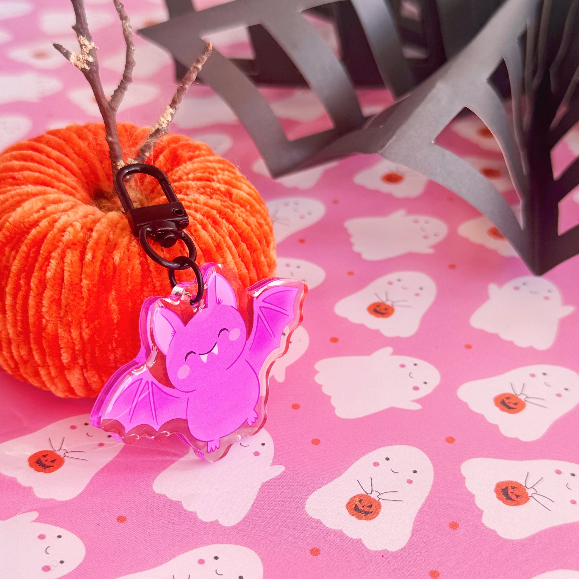 A purple acrylic bat keyring, featuring an illustration of a  cute smiling bat. The keyring has a black clasp to attach it to keys or a bag.