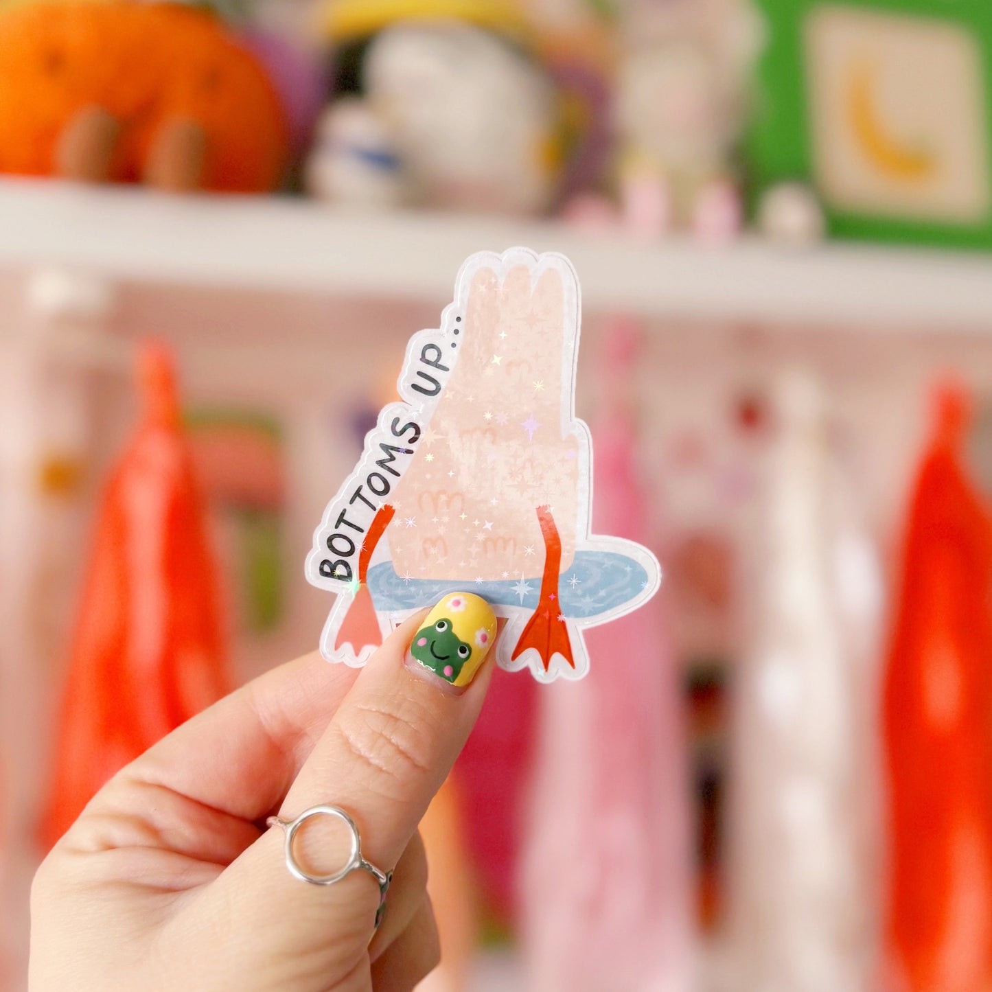 A holographic sticker of a duck upside down in water, with the text - bottoms up, next to it.