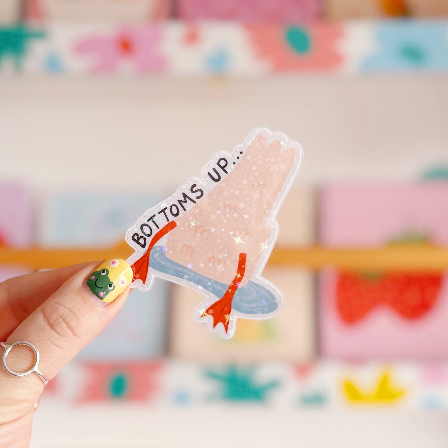 A holographic sticker of a duck upside down in water, with the text - bottoms up, next to it.