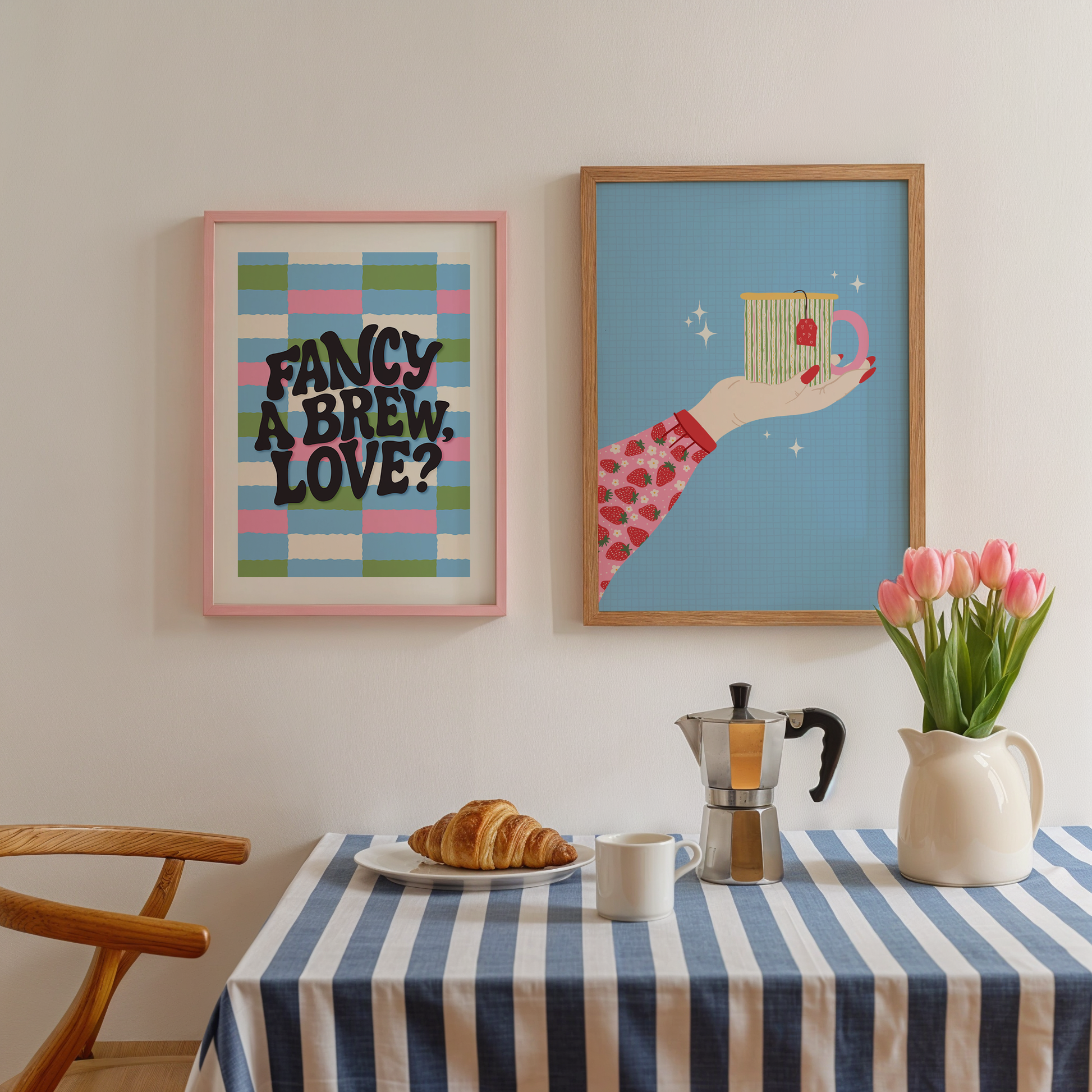 A kitchen scene with two framed prints, one of a colourful checkered background with black text that says 'fancy a brew, love?' and the second is a bright blue print with a hand holding a colourful mug.