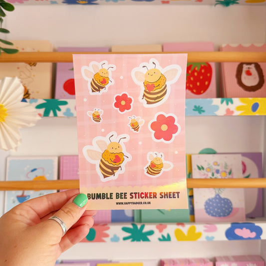 Hand holding a sticker sheet with bumble bee design in front of a colourful shelf.