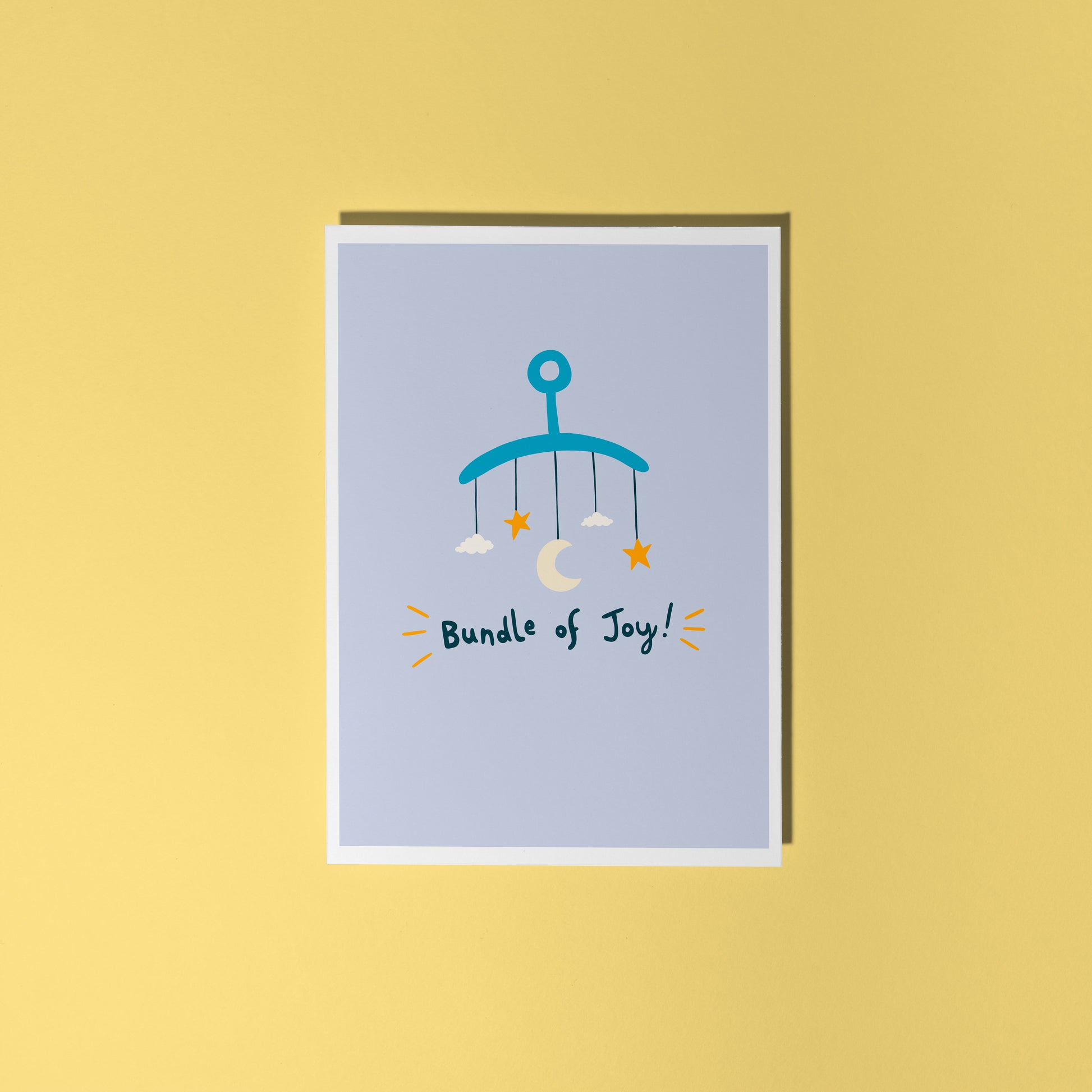 A blue greeting card with an illustration of a mobile. Underneath the illustration is hand written text that reads 'bundle of joy!'.