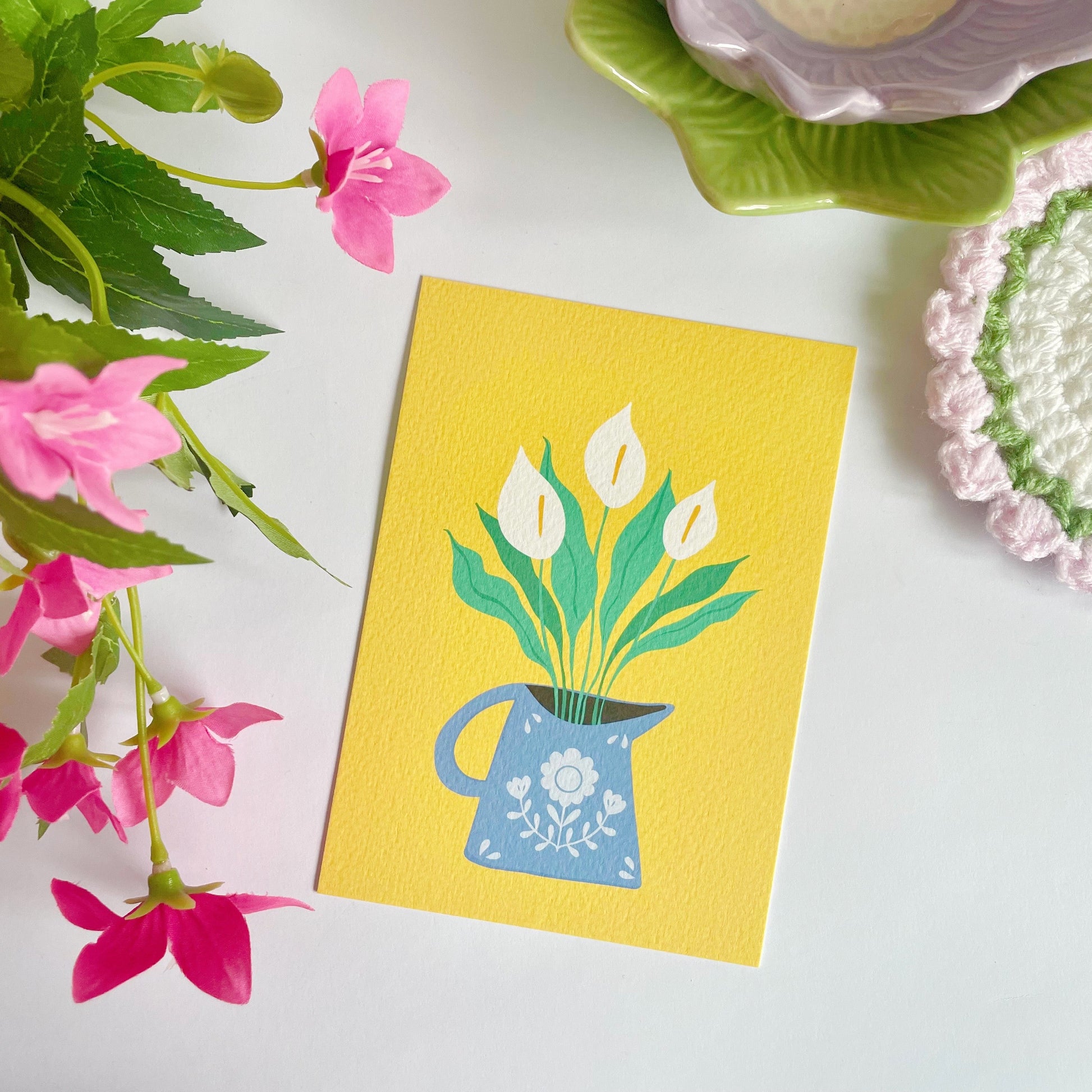 A yellow textured postcard with an illustration of a blue vase with white calla Lillies in it. 