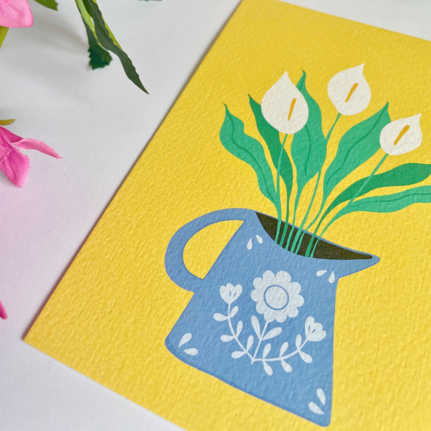 A yellow textured postcard with an illustration of a blue vase with white calla Lillies in it. 