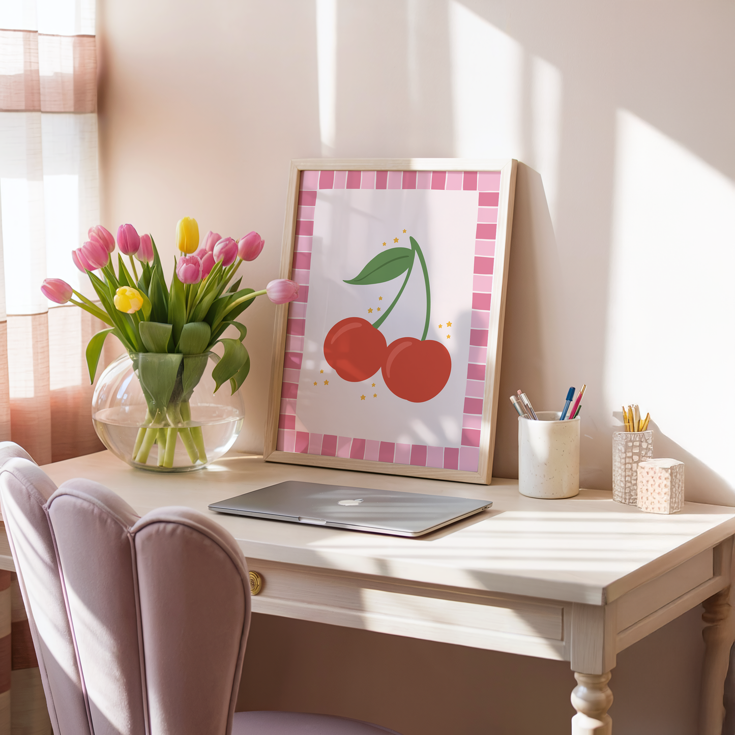 A print with an illustration of a pair of cherries, on a soft pink background surrounded by a bright pink hand drawn border.