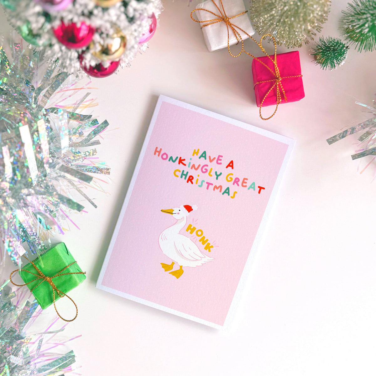 A pink Christmas card with an illustration of a goose with a red Santa hat on. The multicoloured text above the illustration reads 'have a honkingly great Christmas'.