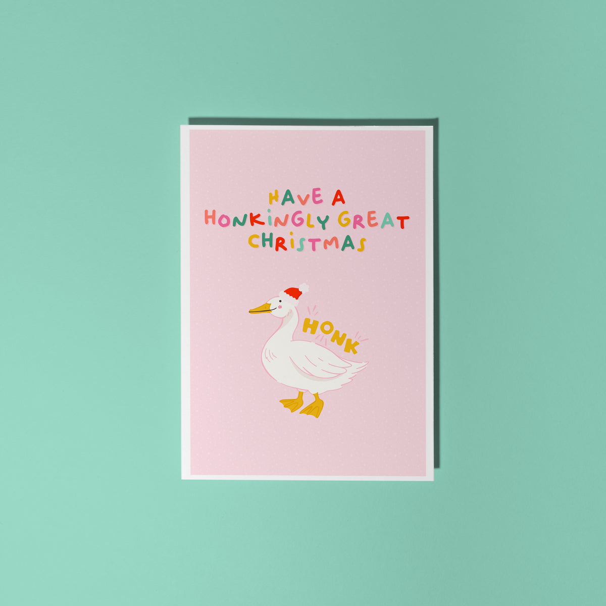 A pink Christmas card with an illustration of a goose with a red Santa hat on. The multicoloured text above the illustration reads 'have a honkingly great Christmas'.