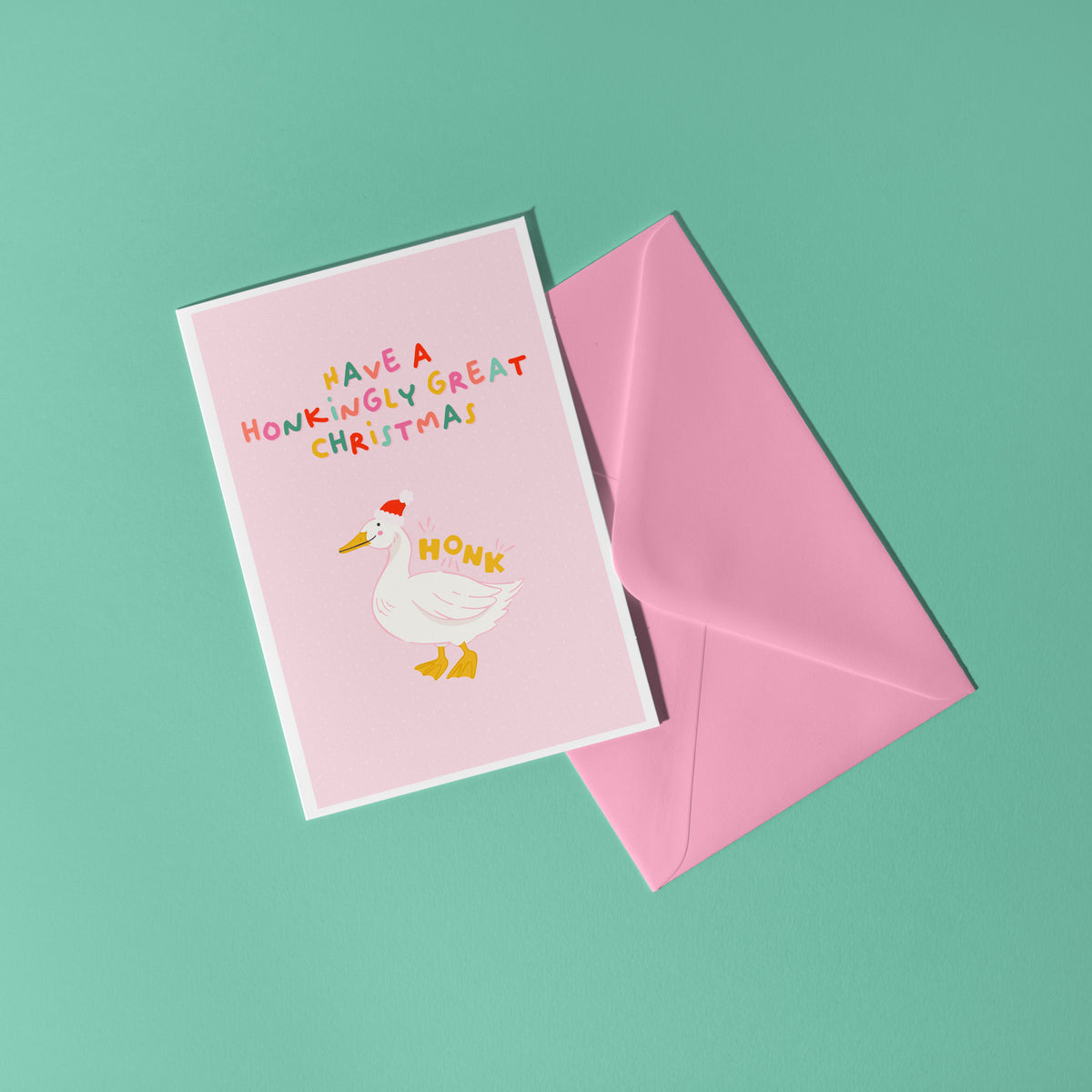 A pink Christmas card with an illustration of a goose with a red Santa hat on. The multicoloured text above the illustration reads 'have a honkingly great Christmas'.