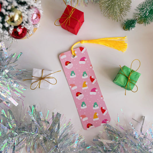 Pink bookmark with Christmas hats pattern surrounded by festive decorations on a white background