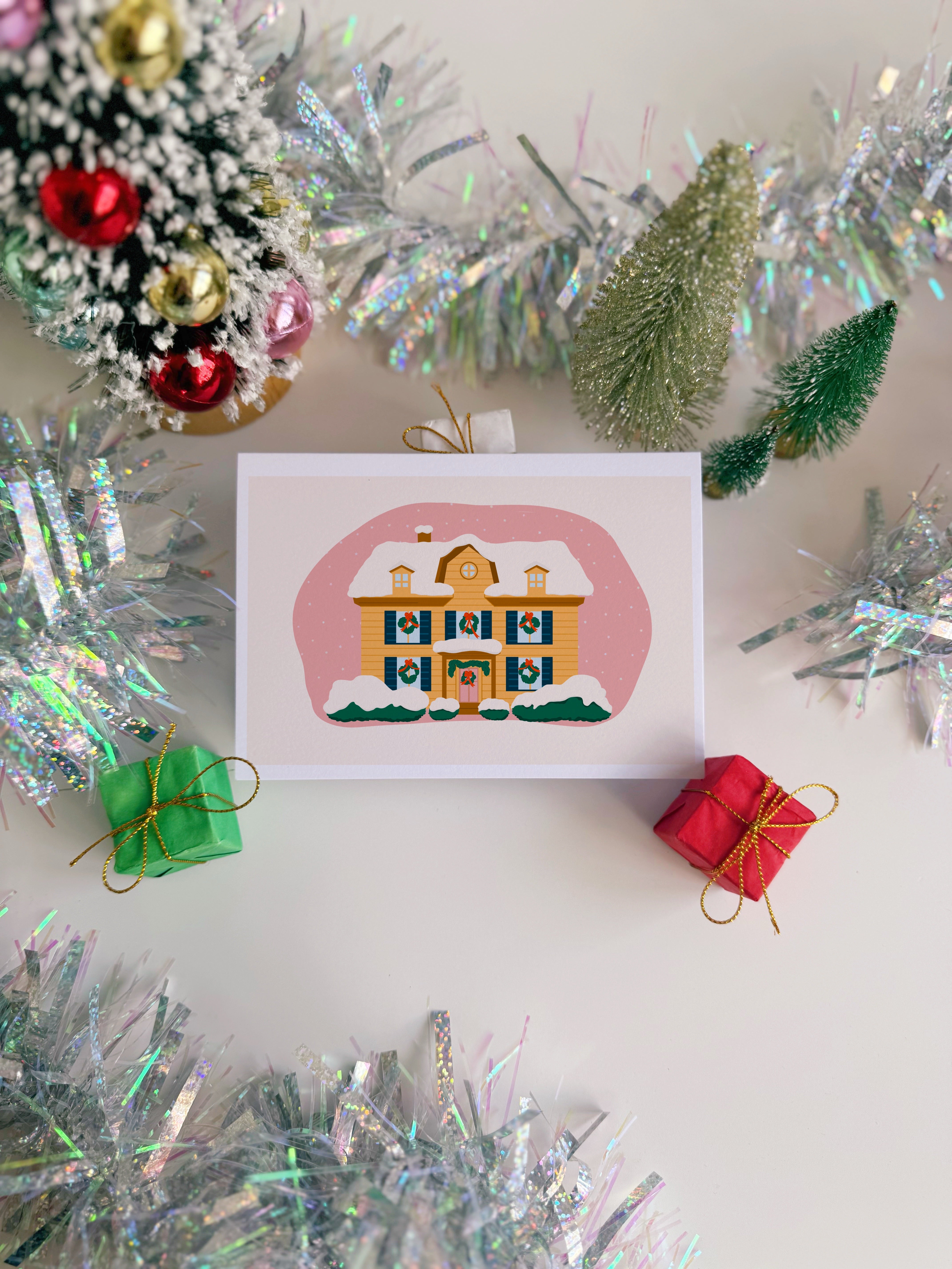 Christmas card with a house illustration surrounded by tinsel and small trees.