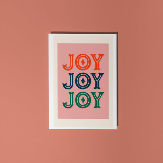 Framed artwork with 'JOY' text in red, blue, and green on a pink background