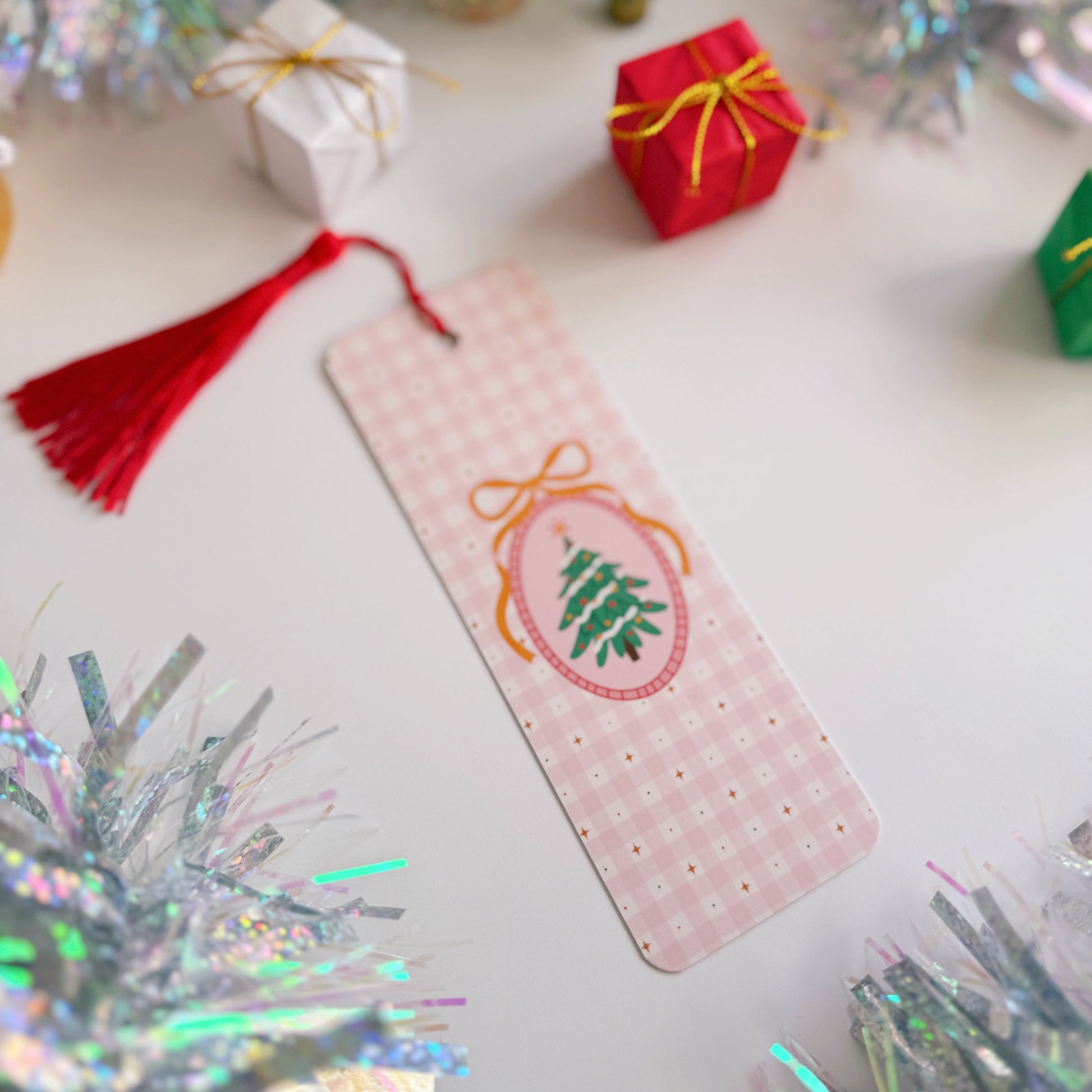 Decorative bookmark with Christmas tree design on a festive background with tinsel and small gift boxes.
