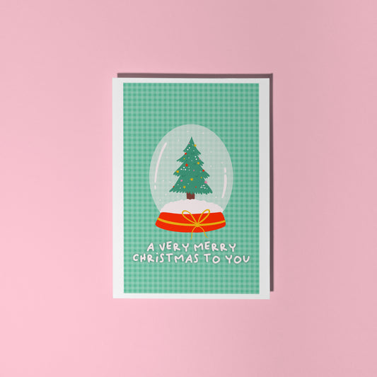 Christmas card with a snow globe design featuring a tree on a pink background