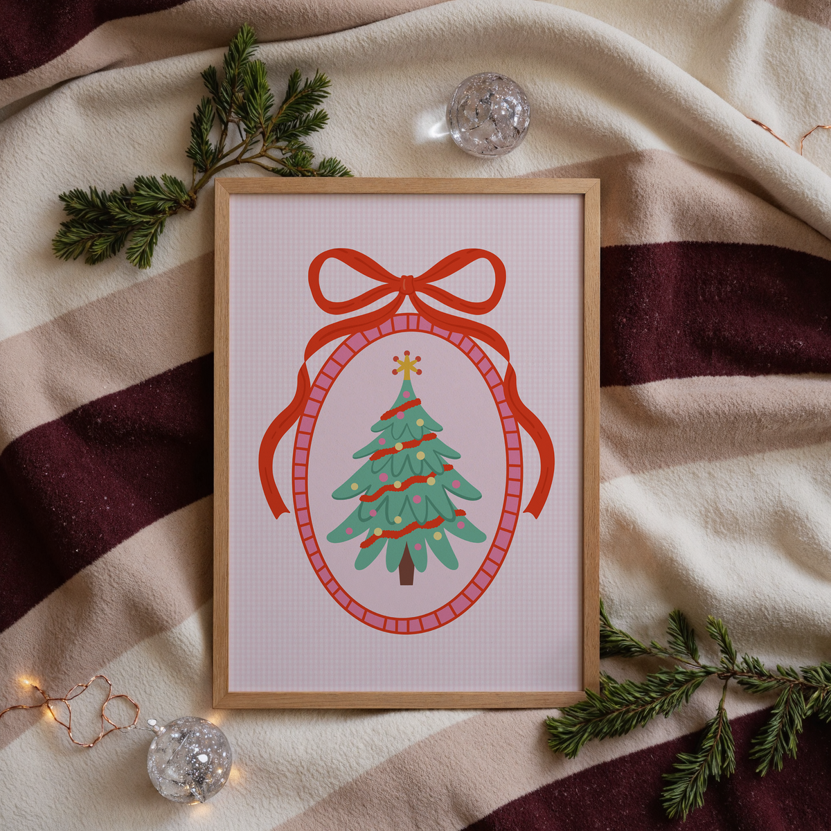 An illustration of a Christmas tree, surrounded by a hand drawn border with a large red bow on top. The background of the print is a soft pink gingham.