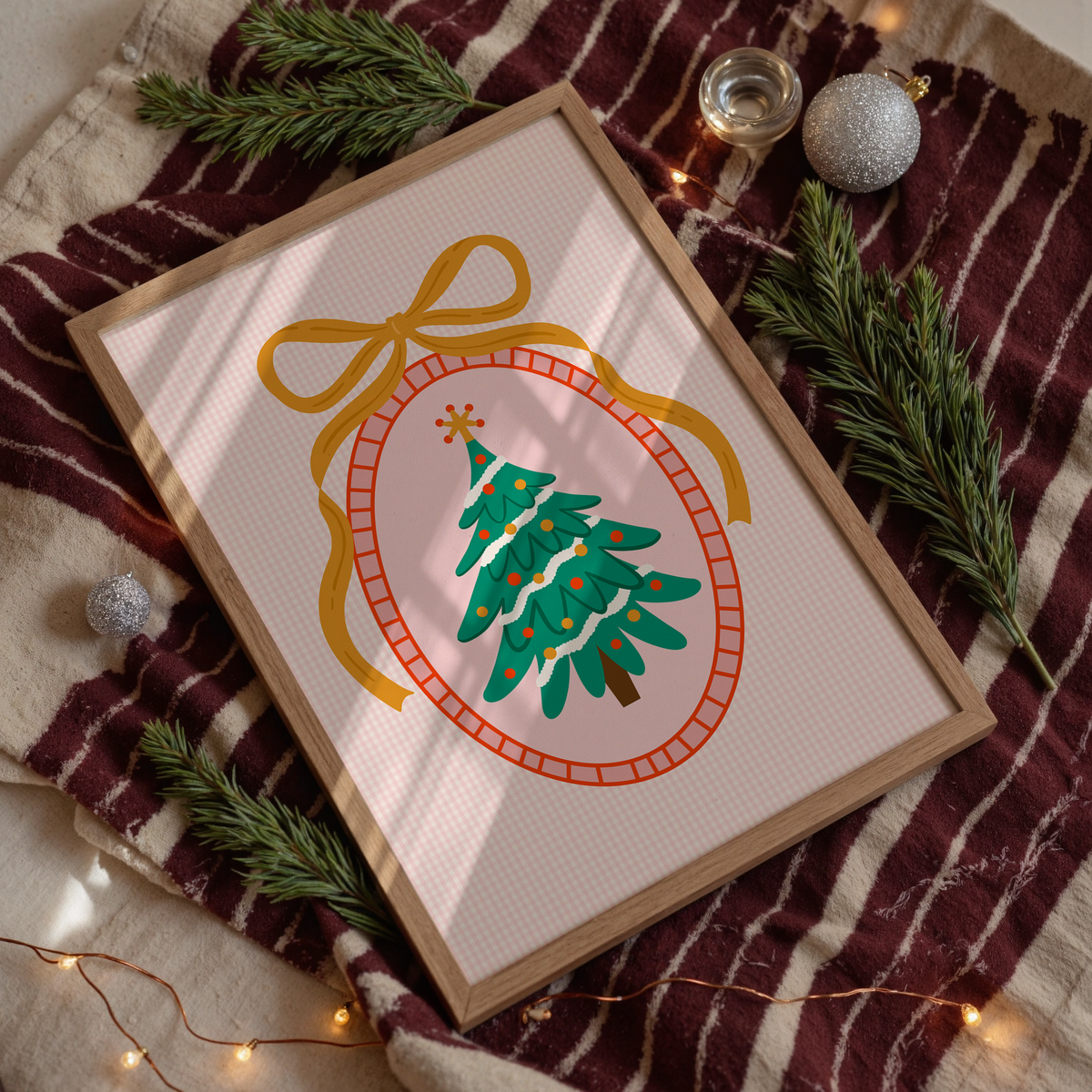 An illustration of a Christmas tree, surrounded by a hand drawn border with a large golden bow on top. The background of the print is a warm pink gingham.
