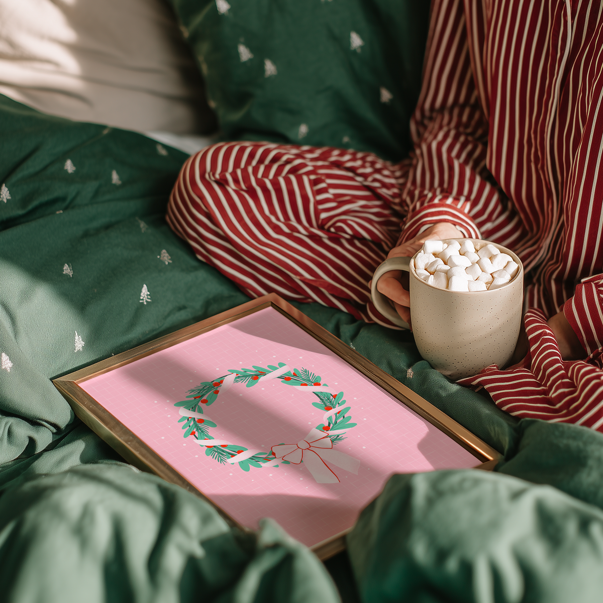 A bright pink christmas print featuring an illustration of a wreath wrapped in ribbon.