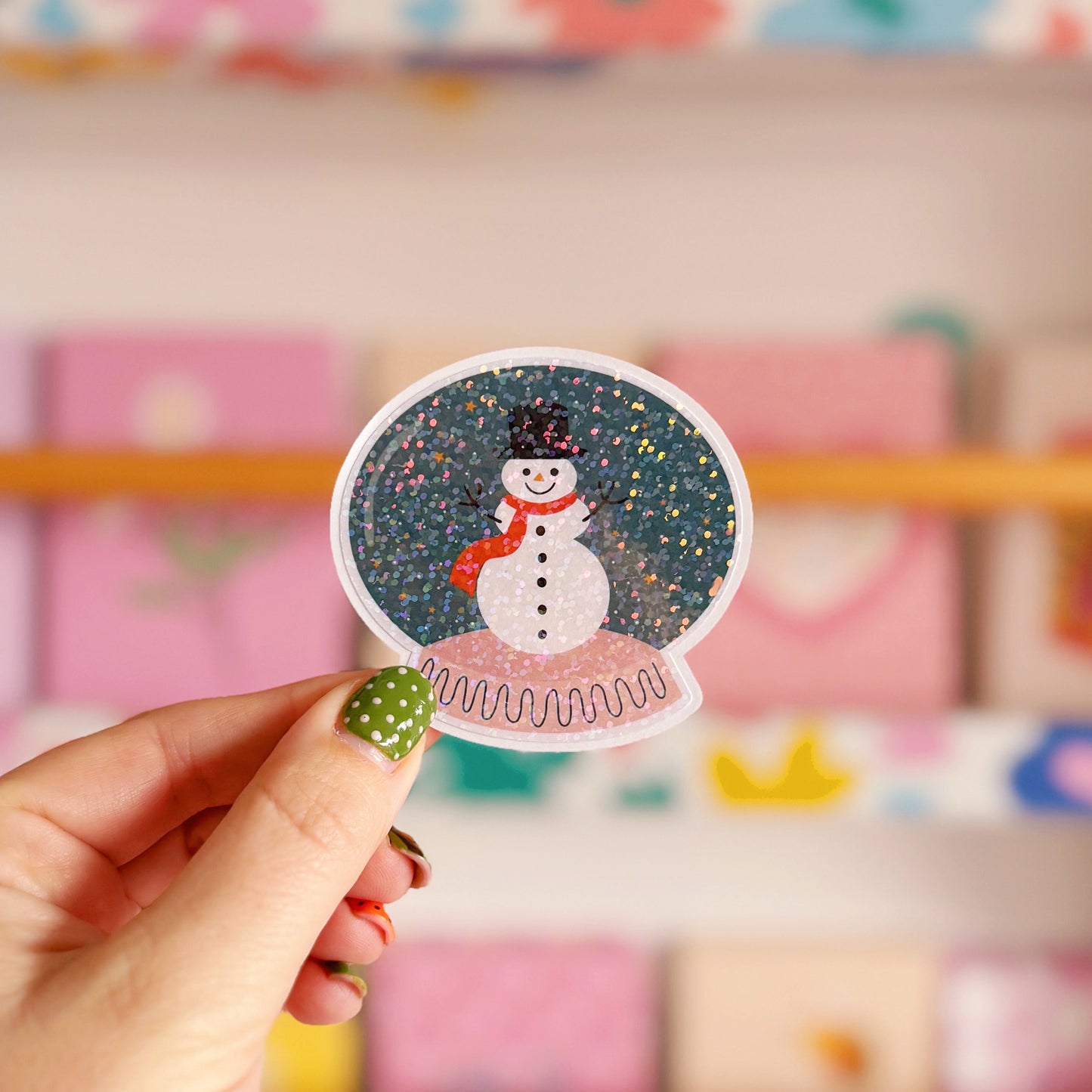 Hand holding a snowman sticker with a colorful background