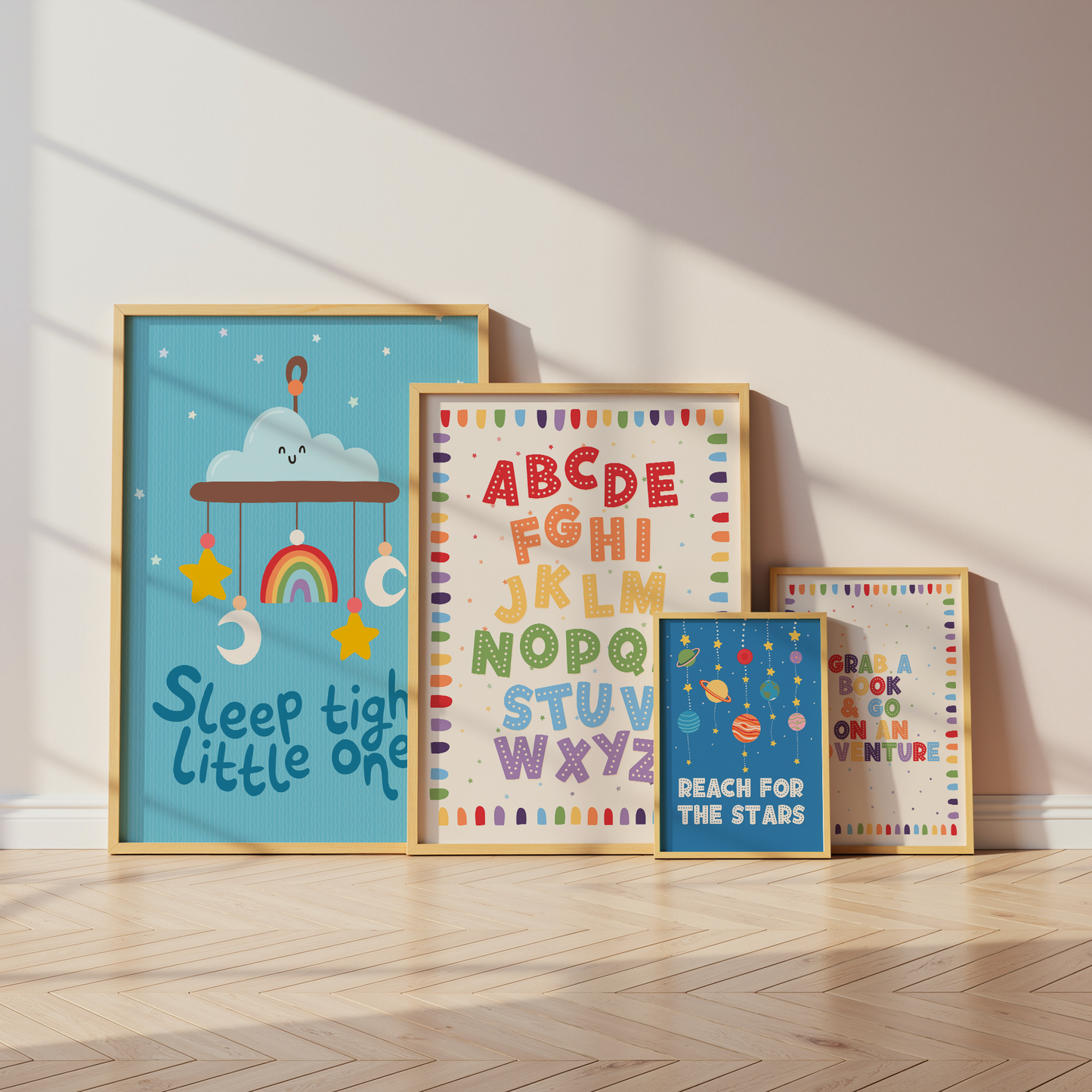 Four framed children's wall art prints leaning against a beige wall on a light wood floor. The largest print says 'Sleep tight little one' with a cloud, rainbow, stars, and moon illustration on a blue background.