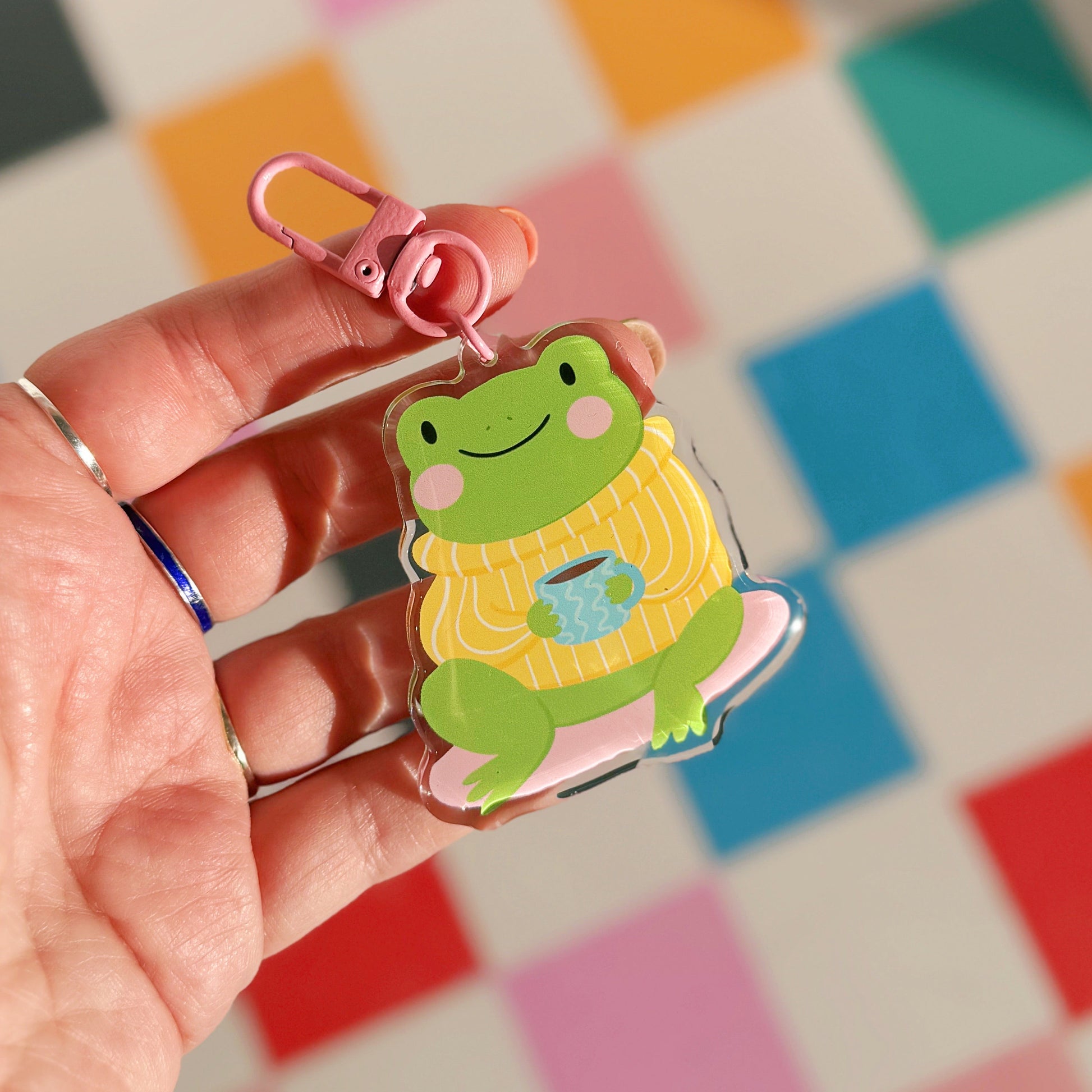 Keychain with a frog design held by a hand against a colorful checkered background