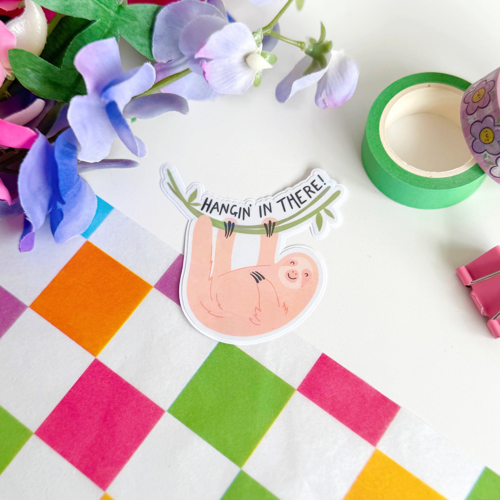 A holographic sticker with a sloth and 'Hangin' in There!' text.