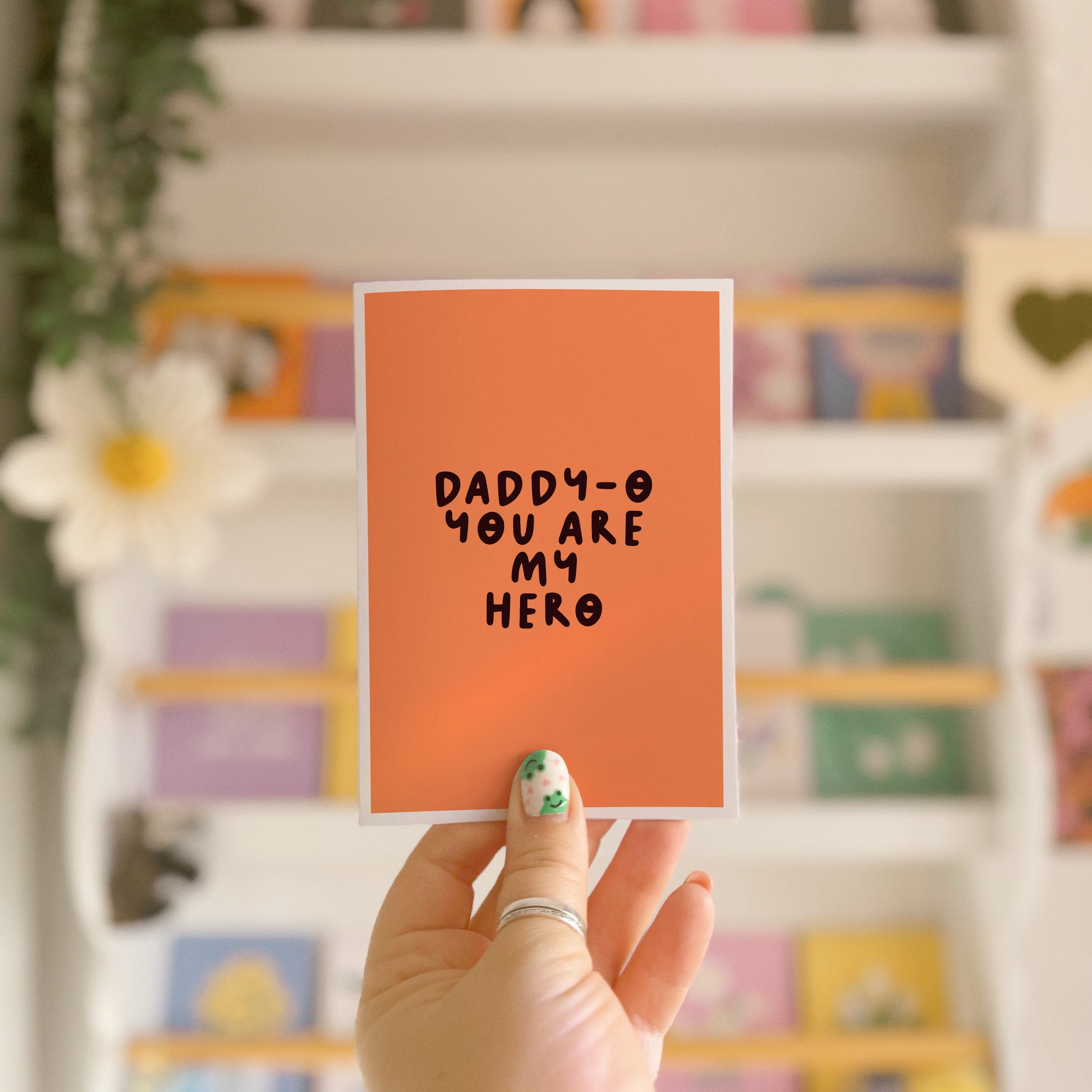 An orange greeting card with text in dark brown that says 'daddy-o you are my hero'.
