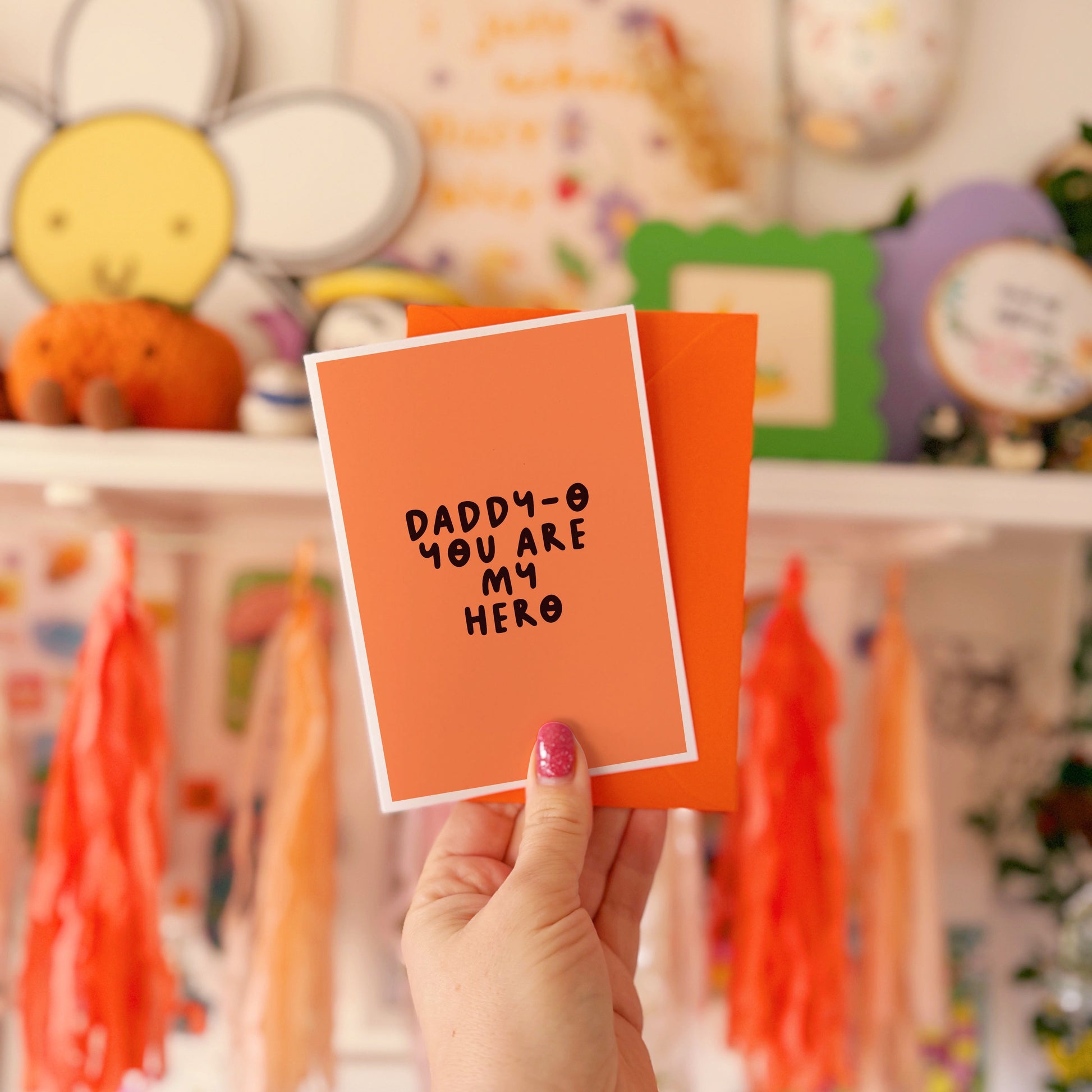 An orange greeting card with text in dark brown that says 'daddy-o you are my hero'.