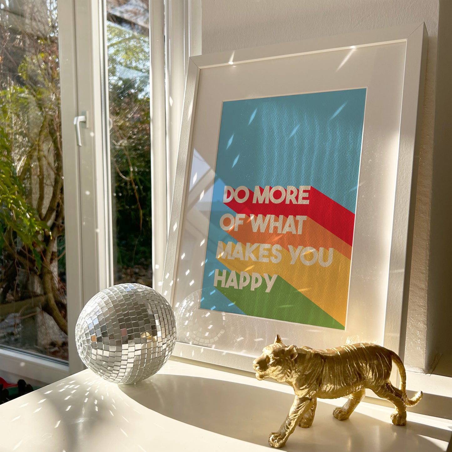 A colourful print, featuring a blue background and white text saying 'do more of what makes you happy' with bold stripes of red, orange, yellow and green behind the text.
