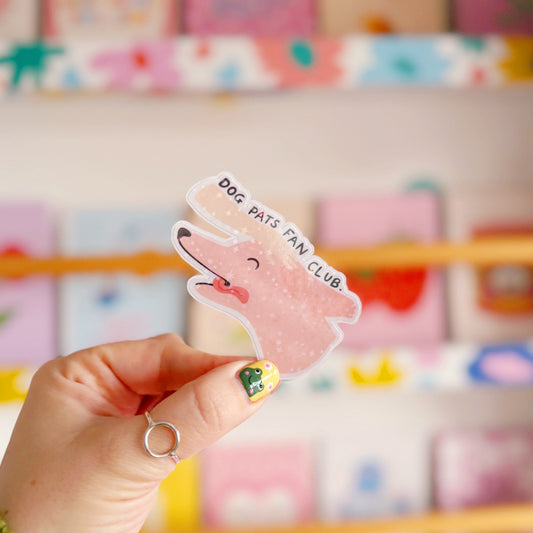 A holographic sticker of a pink dog, with its tongue sticking out, with a hand patting its head. The text reads 'Dog Pats Fan Club.'