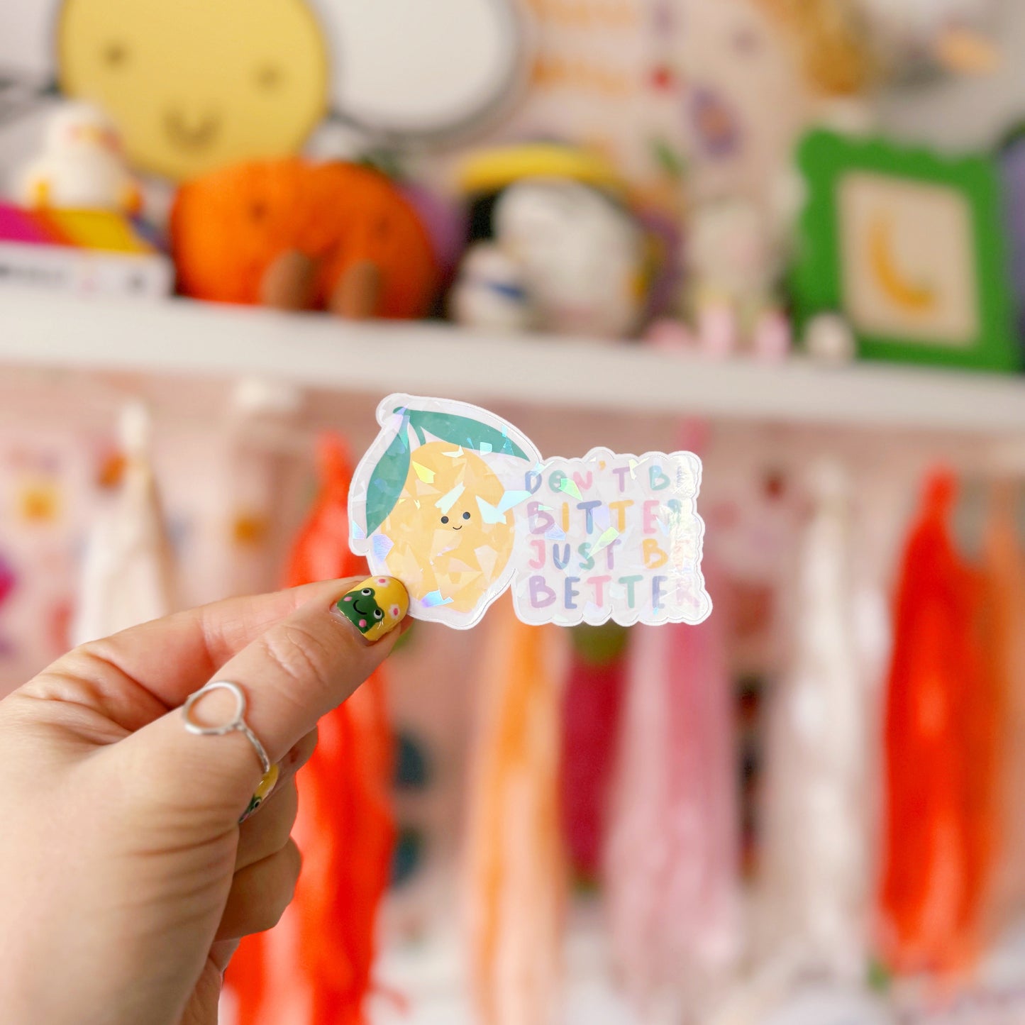 A holographic sticker, of a smiling lemon and the quote don't be bitter just be better. The sticker has an easy peel lip.