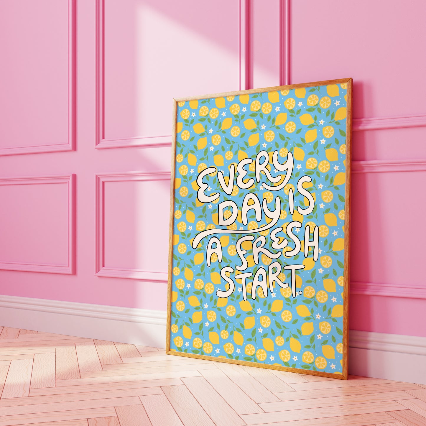 A bright quote print, with hand lettered words reading 'every day is a fresh start' on a blue background with a lemon pattern.