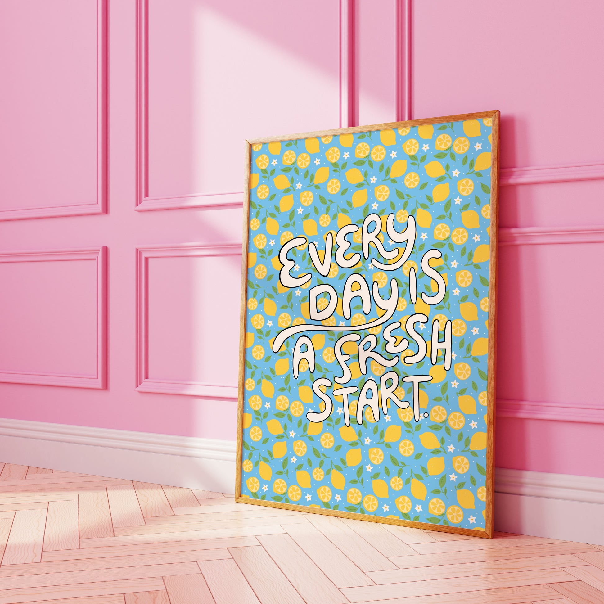 A bright quote print, with hand lettered words reading 'every day is a fresh start' on a blue background with a lemon pattern.