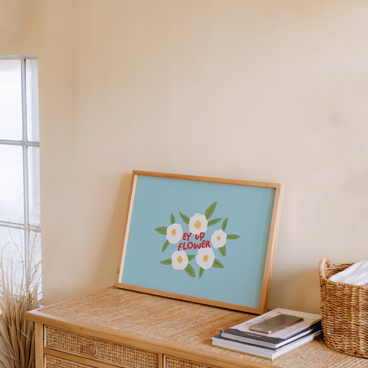 A blue print with illustrations of white flowers surrounding a quote, in red text, that says 'Ey Up Flower'. The print is horizontal orientation.
