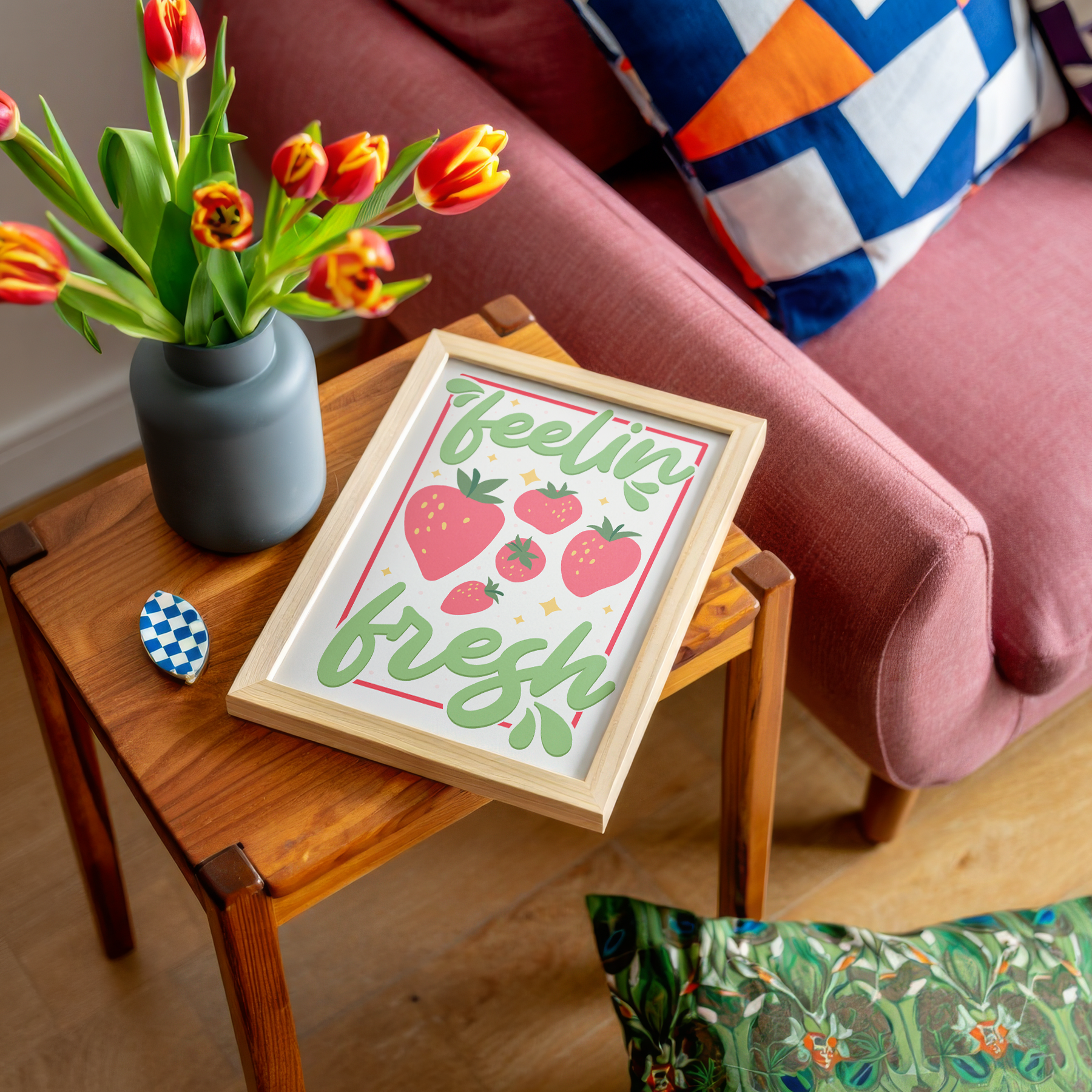 A colourful art print with the phrase 'feelin' fresh' surrounded by illustrations of strawberries, shown in a frame.
