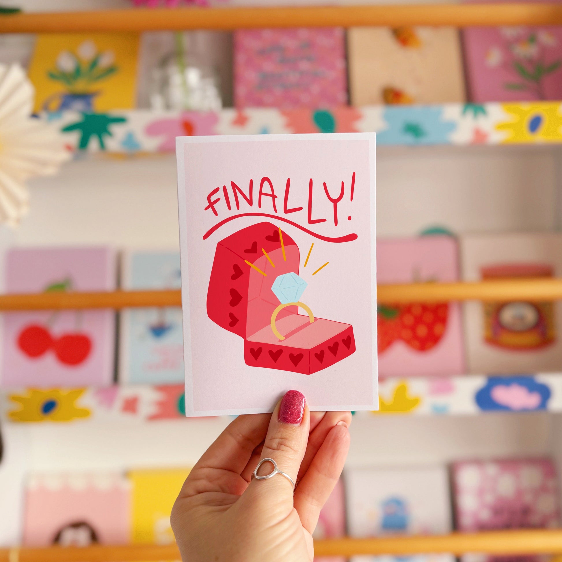 Card with a red engagement ring box and the word 'FINALLY!' on a light pink background.