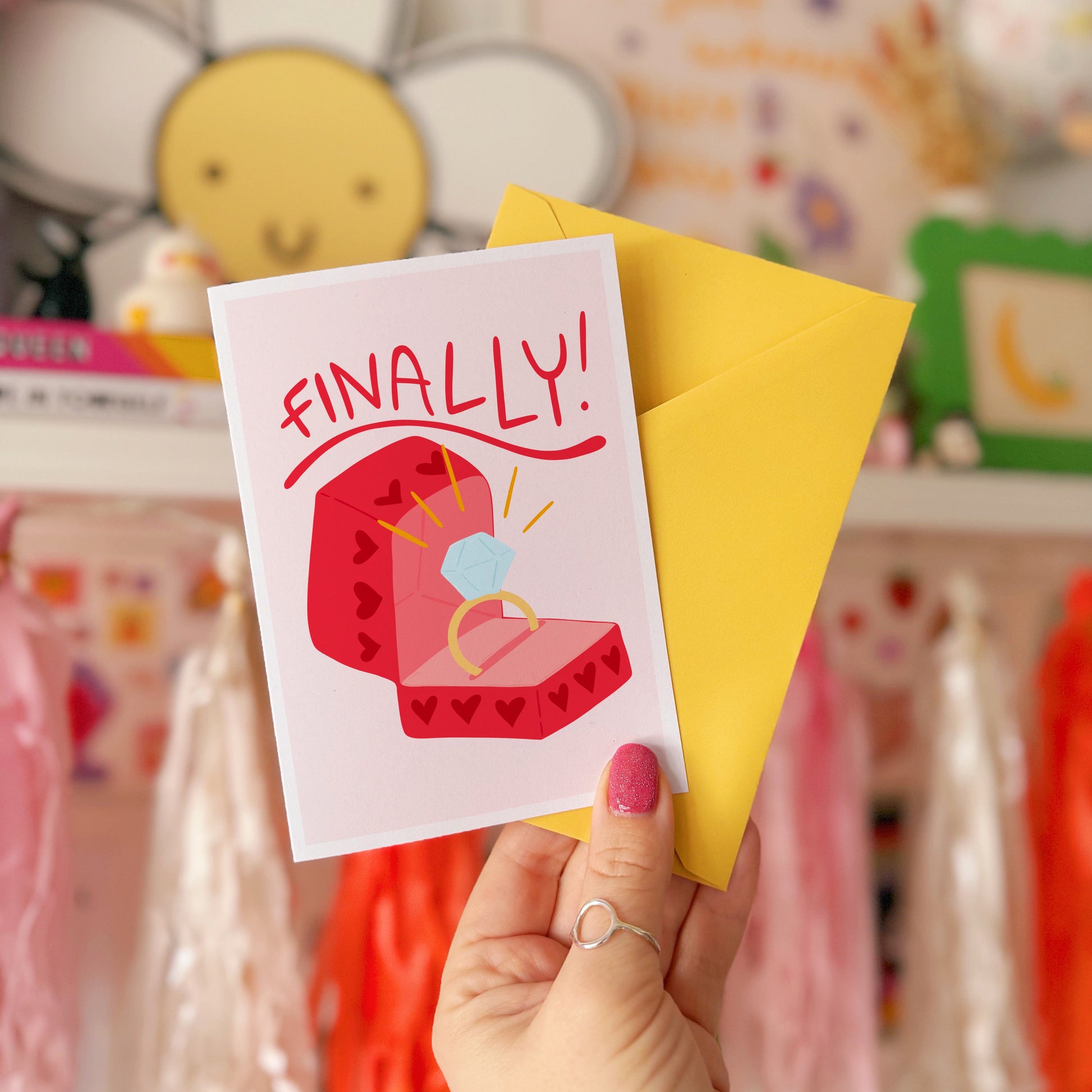 Card with a red engagement ring box and the word 'FINALLY!' on a light pink background.