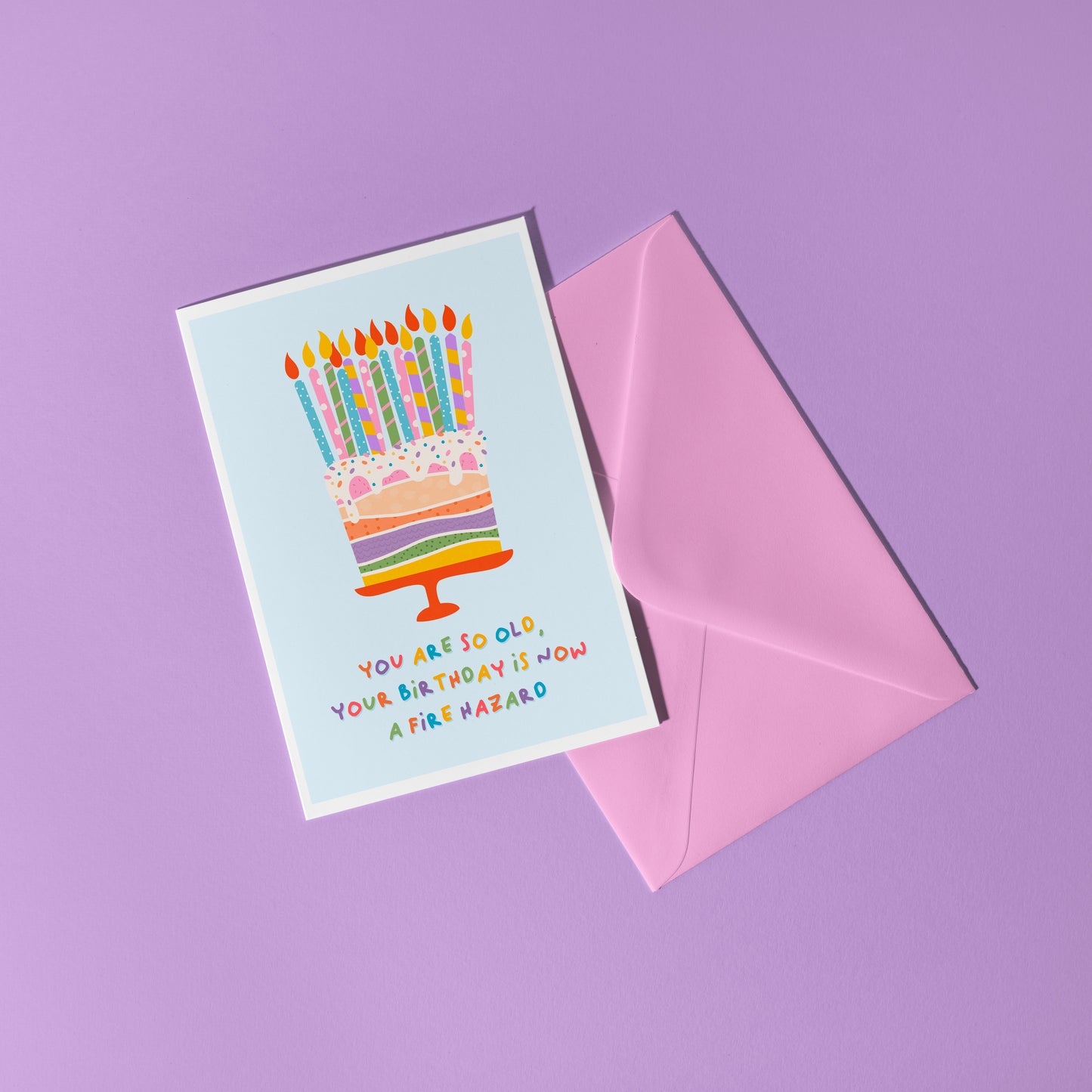 A birthday card with an illustration of a cake, topped with several candles. The text underneath the illustration reads 'you are so old, your birthday is now a fire hazard'.
