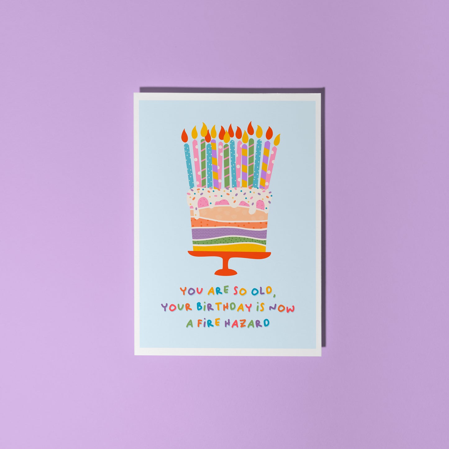 A birthday card with an illustration of a cake, topped with several candles. The text underneath the illustration reads 'you are so old, your birthday is now a fire hazard'.
