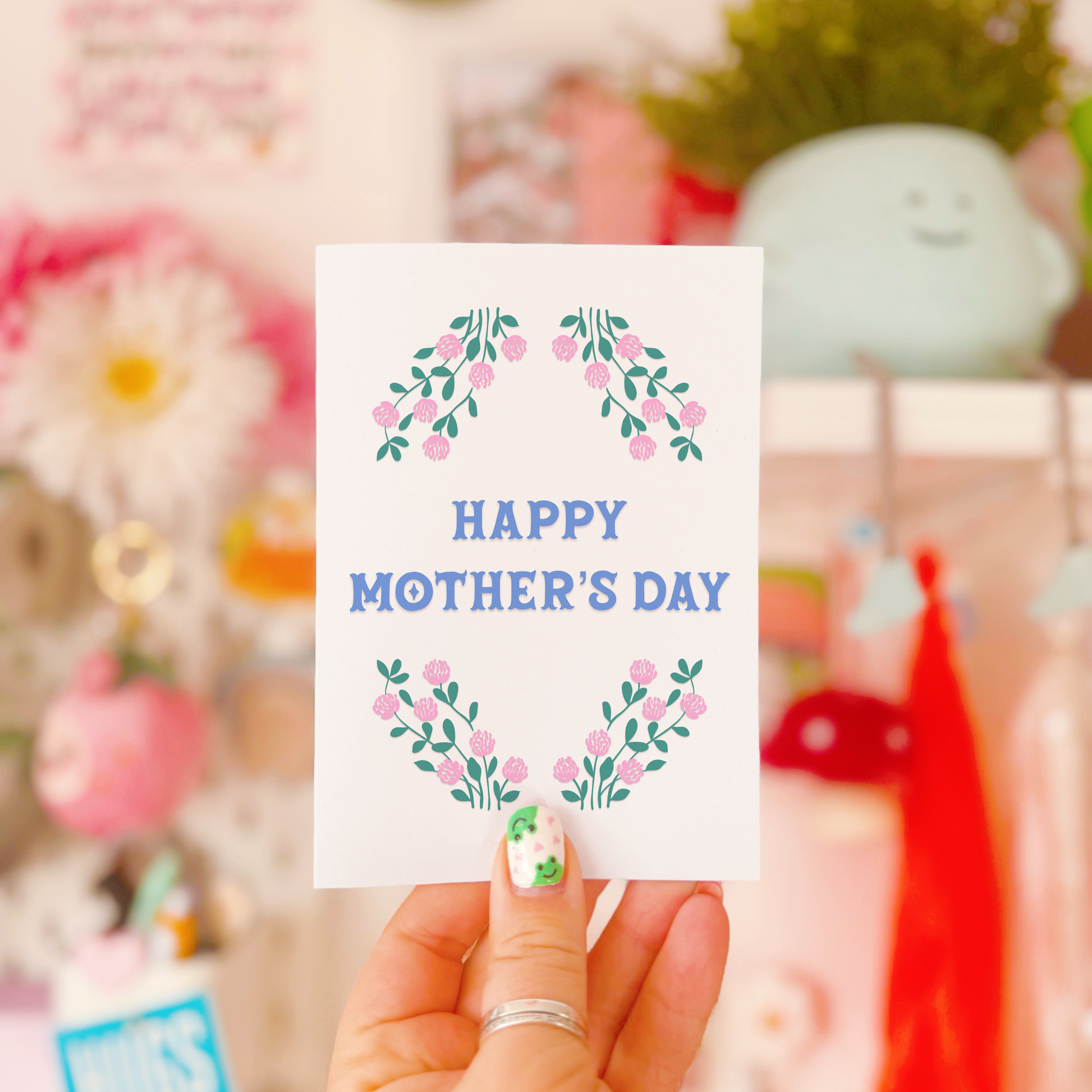 A Mother's Day card, with a pink and green floral border and the words 'Happy Mother's Day' written in the centre in blue.