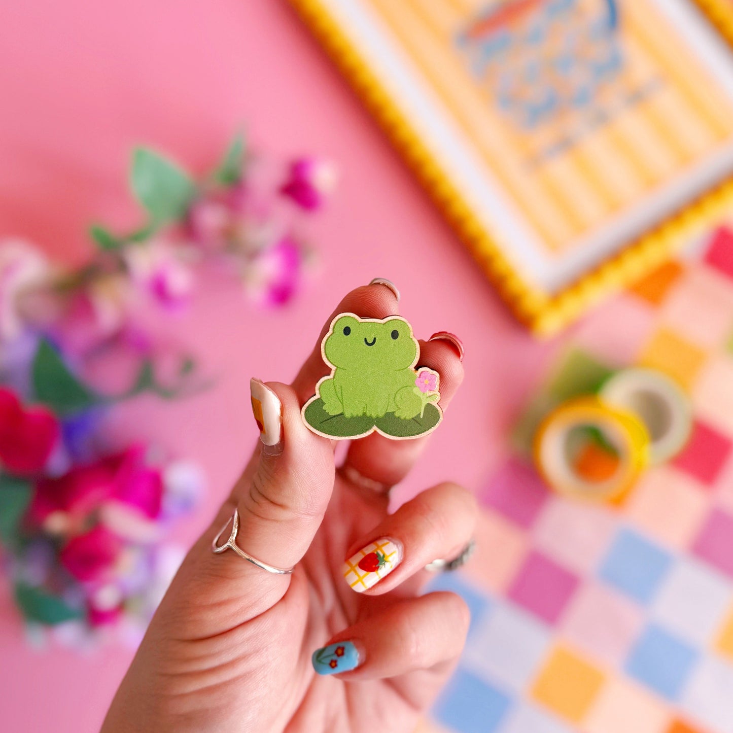 A cute green frog pin badge, made out of wood with two metal clasp fastenings to the back.