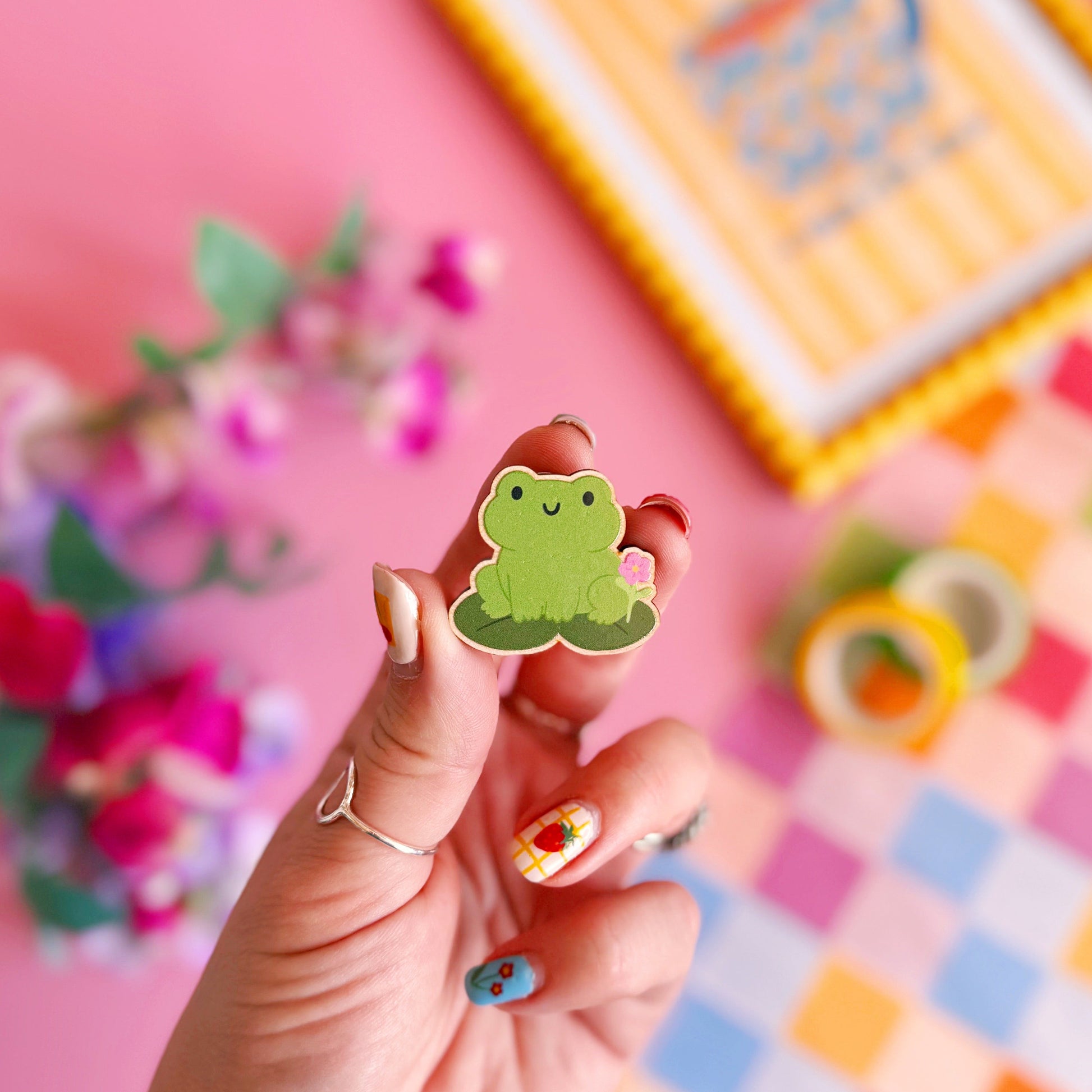 A cute green frog pin badge, made out of wood with two metal clasp fastenings to the back.