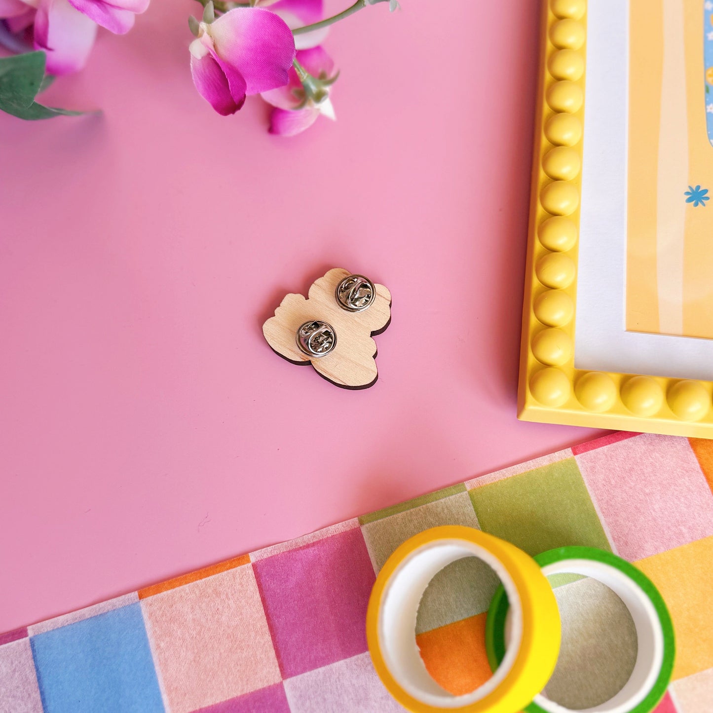 A cute green frog pin badge, made out of wood with two metal clasp fastenings to the back.