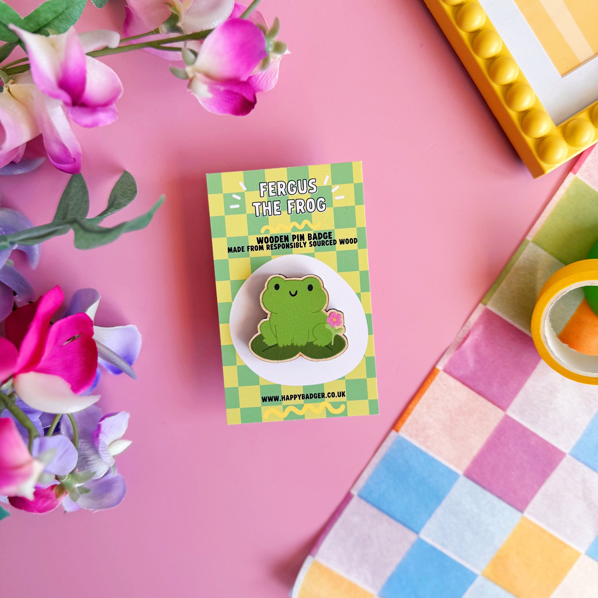 A cute green frog pin badge, made out of wood with two metal clasp fastenings to the back.